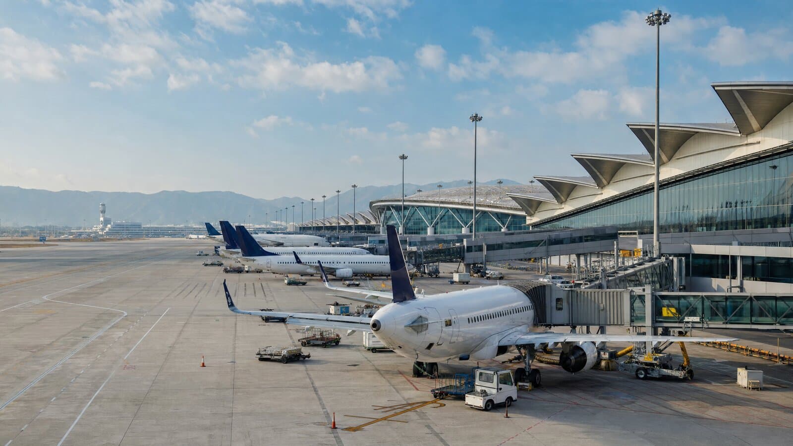 Commercial airplanes parked at a busy airport terminal under clear sky